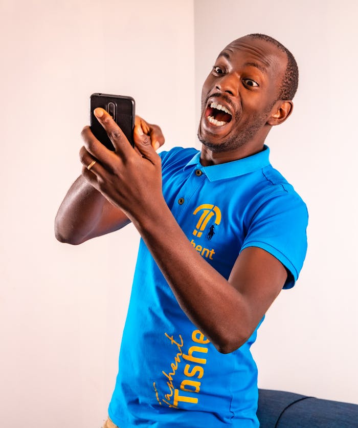 African American man in blue polo shirt enjoying game on smartphone with excitement indoors.